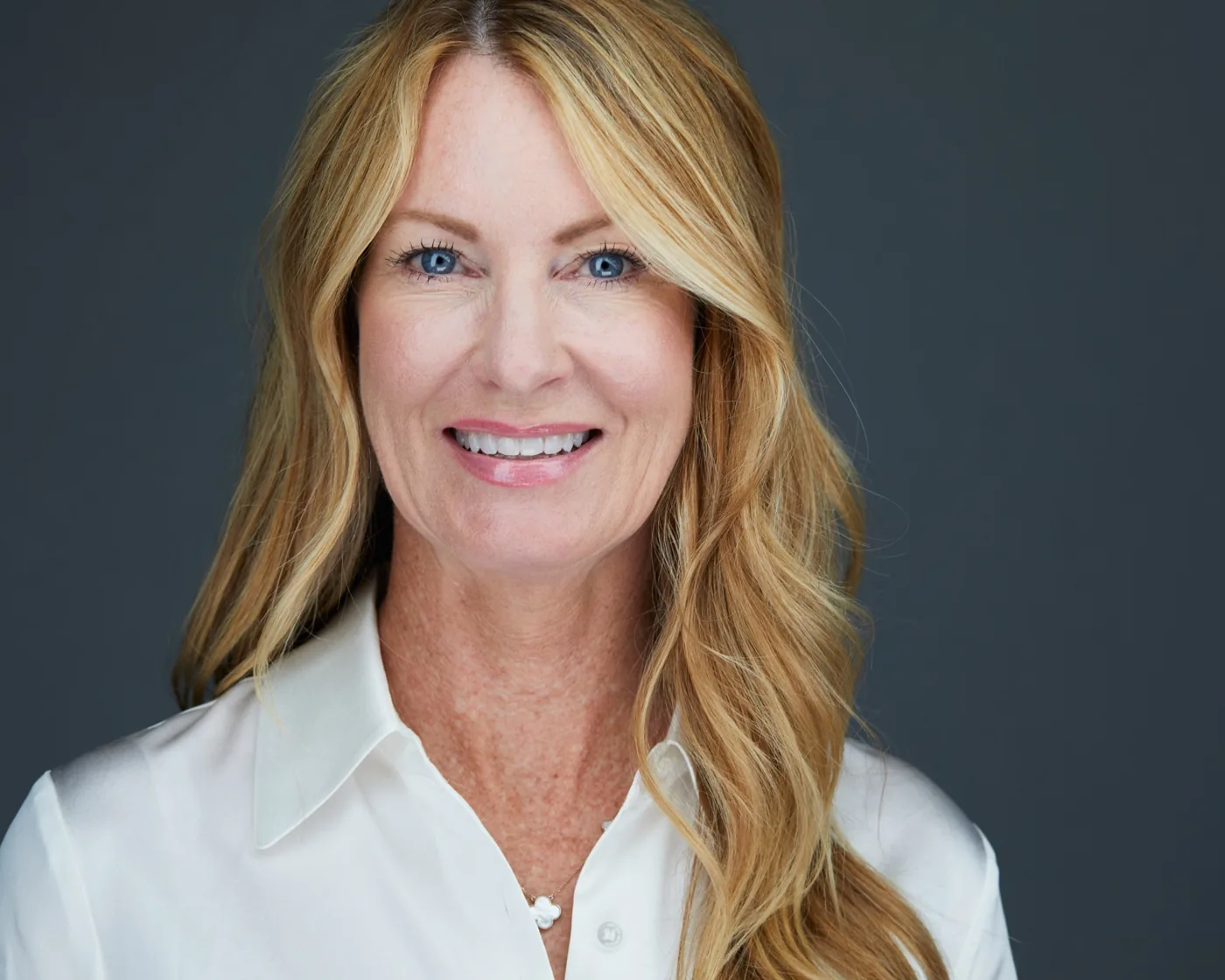 Business headshot of a smiling woman with long blonde hair in a white blouse