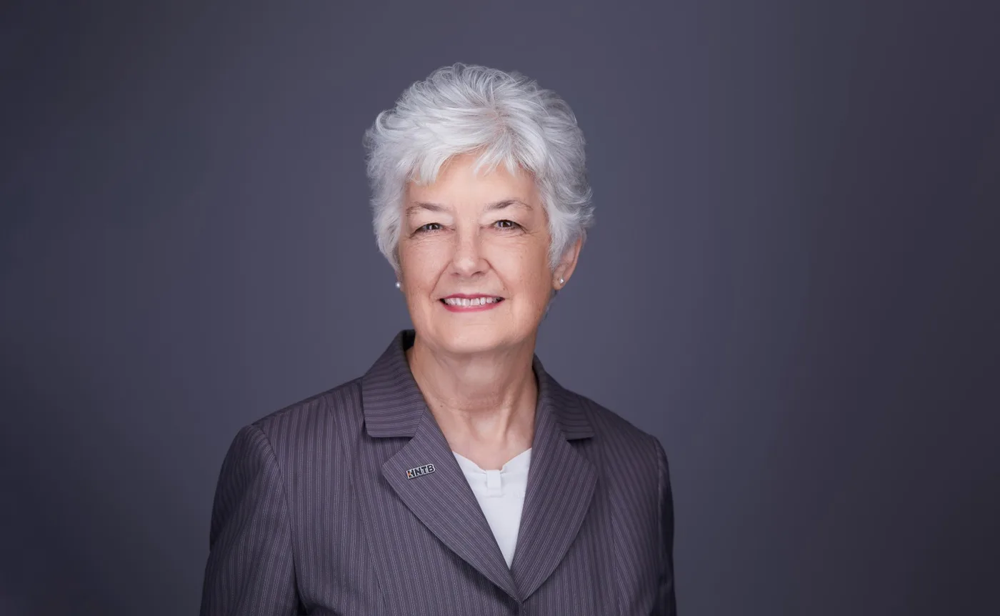 Corporate team headshot of a woman with short silver hair in a gray pinstripe jacket against a gray backdrop