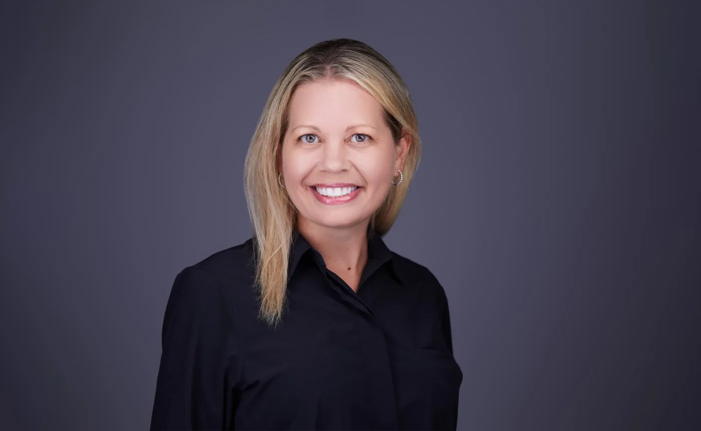 Corporate team headshot of a woman with long blonde hair in a black shirt against a gray backdrop