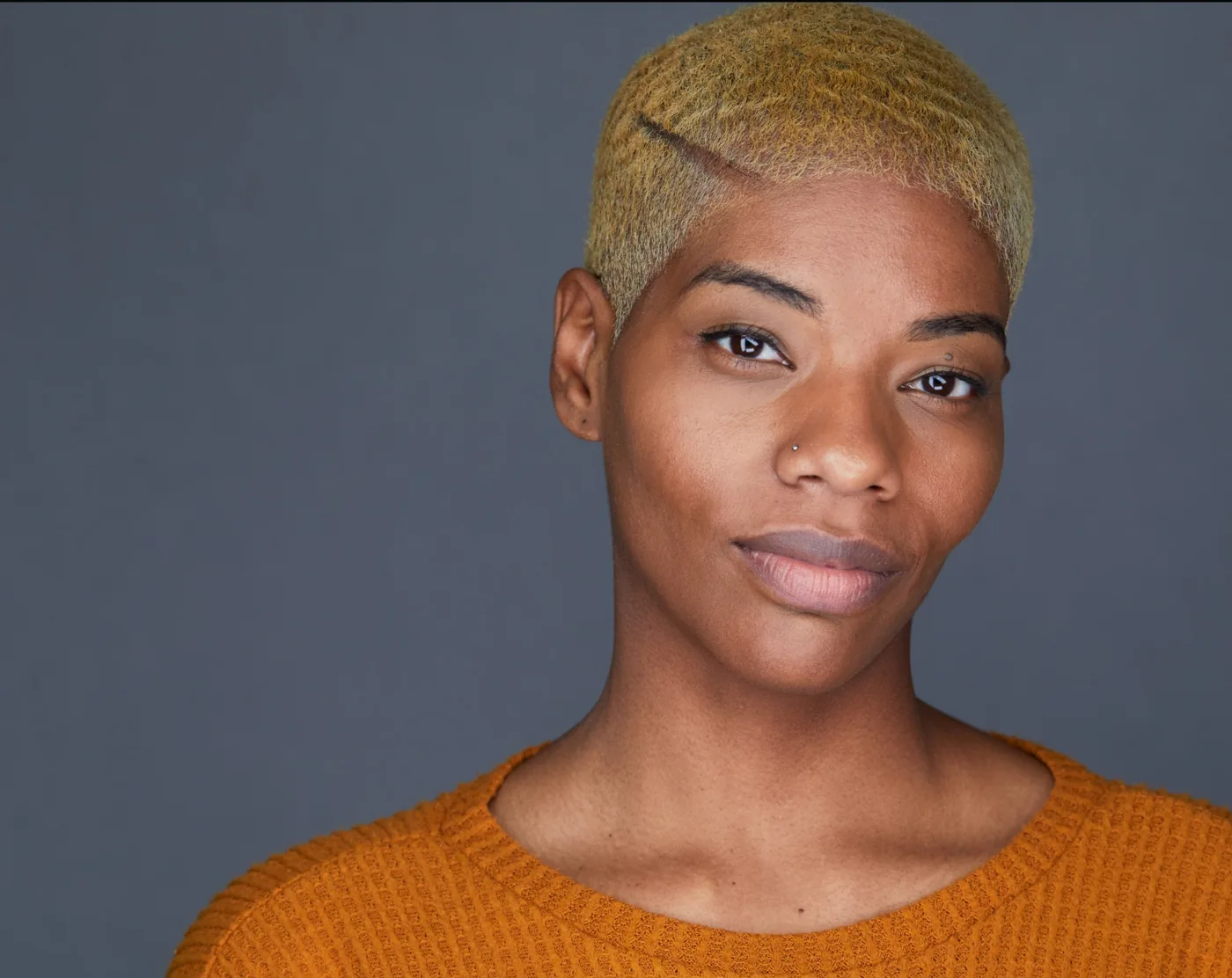 Actor headshot of a woman with short bleached hair in an ochre sweater