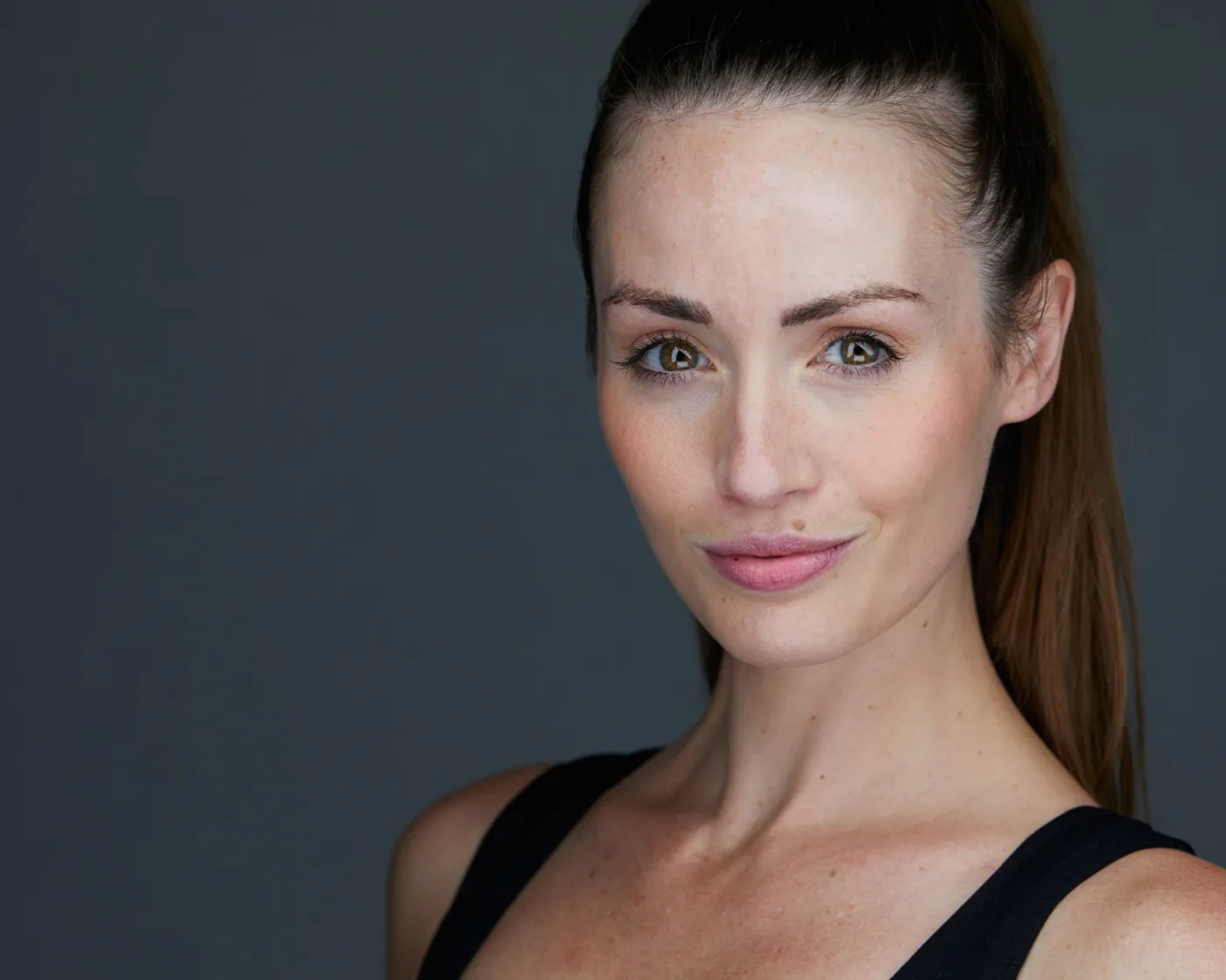Actor headshot of a woman with her hair pulled back, looking straight at the camera
